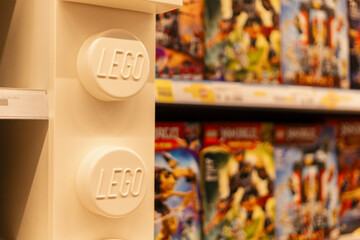 Fototapeta premium Chemnitz, Germany - March 14, 2026: A shelf features a large LEGO block with the brand name. Behind it, various LEGO sets are arranged neatly. Customers browse the selection in a retail store