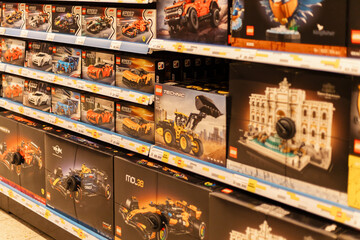 Fototapeta premium Chemnitz, Germany - March 14, 2026: Shelves in a retail store show many Lego building kits for sale. The kits include cars, buildings, and construction vehicles. Shoppers browse the toy section