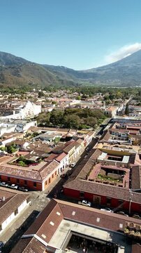 Aerial drone view of a colonial street in Antigua Guatemala aligned with Volcan de Agua rising in the distance. Vertical