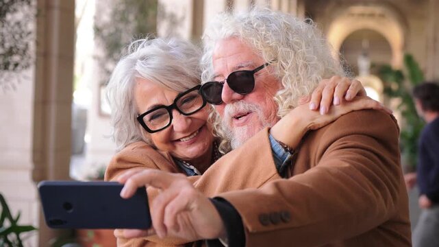 A cheerful elderly couple capturing a joyful moment together as they take a fun selfie with their smartphone, showcasing their happiness and connection in a lighthearted and affectionate manner.
