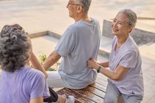 A senior woman massages a man's back while another stands beside them, chatting happily