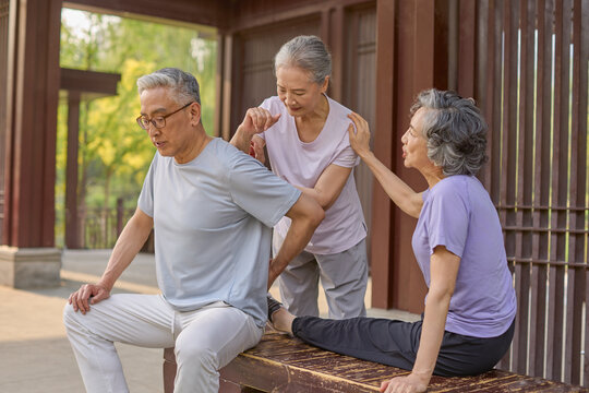 A senior woman massages a man's back while another stands beside them, chatting happily