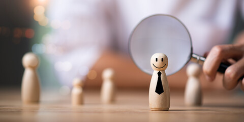 A magnifying glass focuses on a wooden figure with a smile and tie, symbolizing talent selection,...
