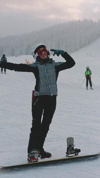 Woman enjoy winter holiday vacation on ski resort. Snowboard girl listen music, dancing and have fun, ski slope, snow covered forest in background. Active sport. Bukovel, Carpathian mountains, Ukraine