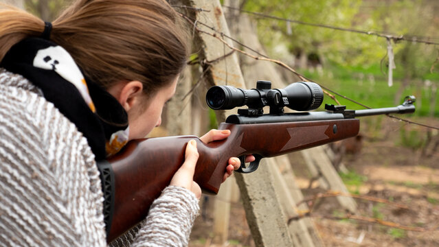 A woman focuses on her target while holding a rifle at an outdoor shooting range. The scene captures her concentration as she prepares to take a shot.