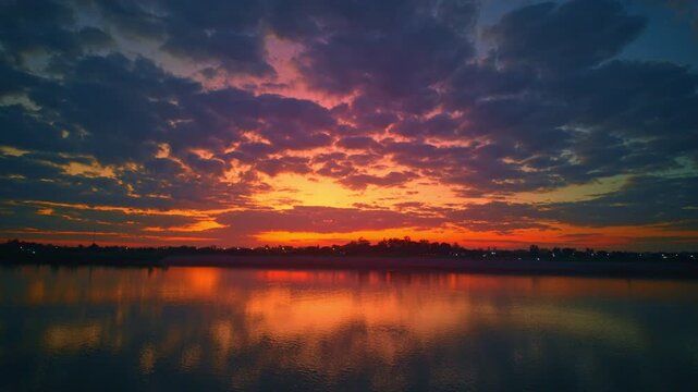 An aerial hyper lapse Golden Light Across Fields and River at Dusk. Warm orange and golden tones reflect on the water as agricultural fields and countryside plains glow beneath a cloud filled sky.