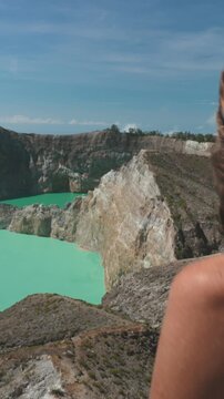 Vertical Screen Video. Tourist enjoy aerial view volcano crater blue lakes. Female traveler stand on mountain top look wild nature scene. Outdoor lifestyle travel on summer holiday vacation. Kelimutu