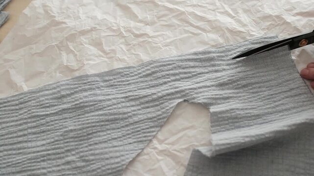 Close up of female hands carefully cuts blue cotton muslin fabric with scissors. Minimal sewing environment, highlighting manual sewing manufacture. Working process in a small business sewing workshop