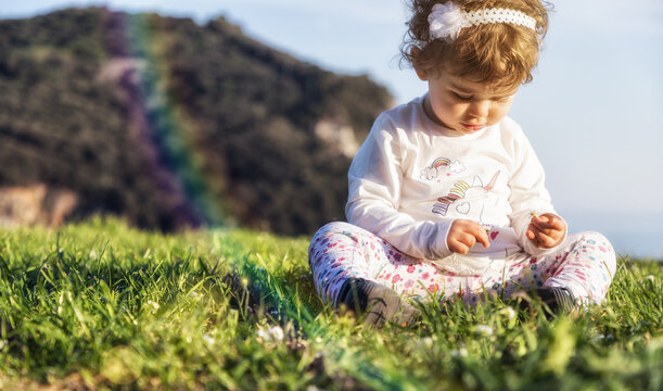 Neonata bionda seduta sul prato illuminata da un bel sole di primavera