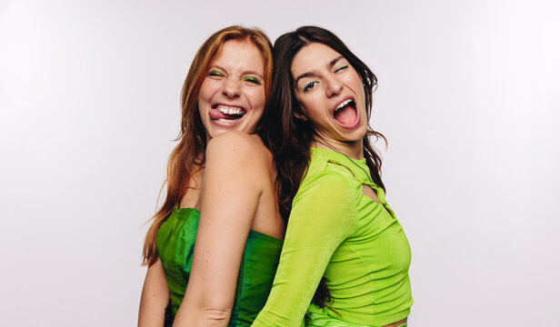 Two friends laugh and wink back to back
