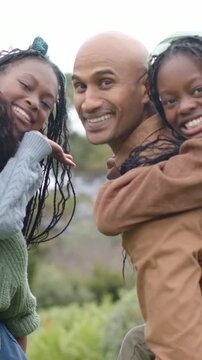 Vertical video: Posing adult with girls widening smiles in park with brown jacket, green knit, bow