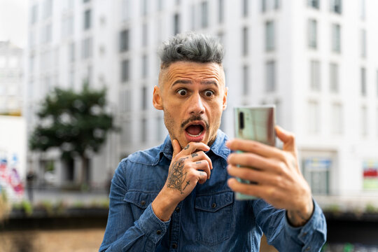 Shocked man holding smart phone during video call against building