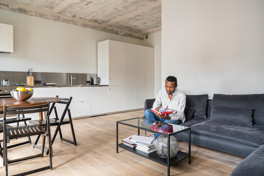 Man sitting on couch in modern apartment turning pages in a book