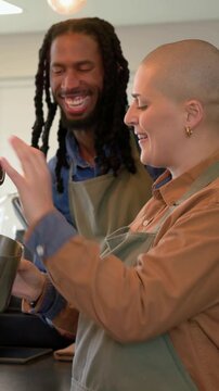 Vertical video: Placing pitcher under wand, trainer in apron training trainee steaming milk at cafe