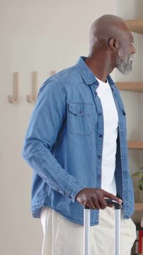 Vertical video: Entering older man holding wheeled case handle checking entry and pointing at hat