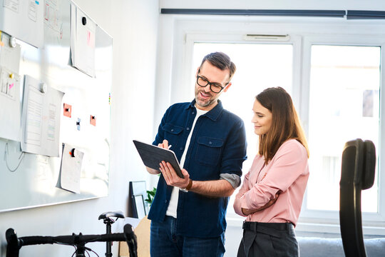Two colleagues at whiteboard sharing tablet in office