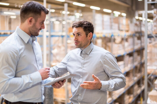 Two men with tablet talking in factory warehouse