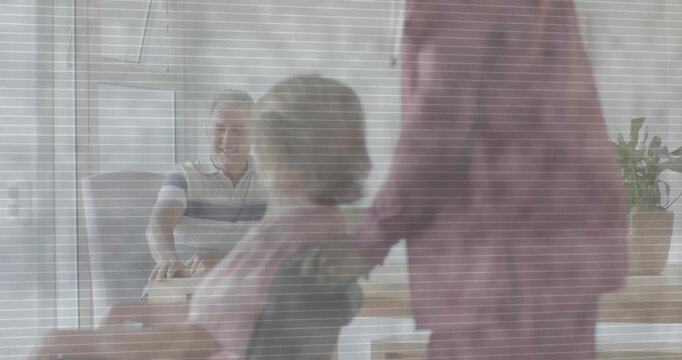 Caregiver pushing senior past desk, laptop, staff noticing, walking toward glass door escorting