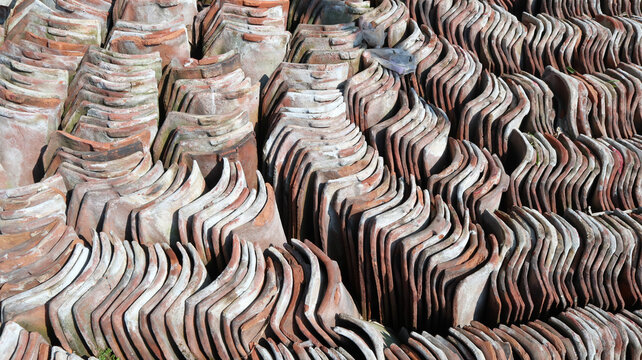 Rows of weathered terracotta roof tiles neatly stacked outdoors, creating an intricate texture and pattern