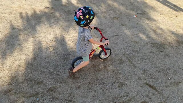 Little boy learning to ride balance bike on a sunny day in the park, developing coordination and motor skills while enjoying outdoor childhood activity and freedom