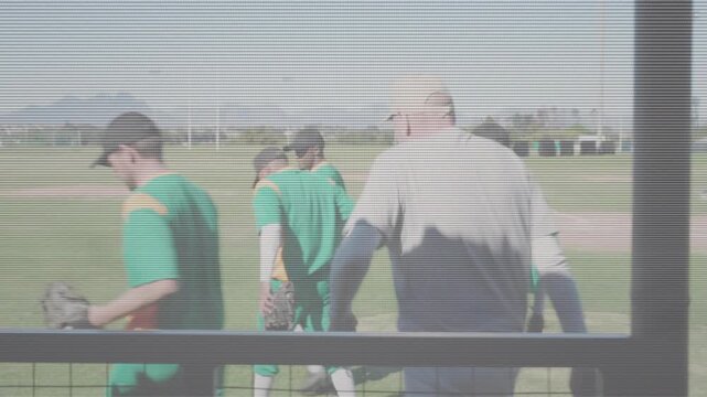 Coach leading team exiting dugout onto sunlit field forming baseball huddle swapping gloves pregame