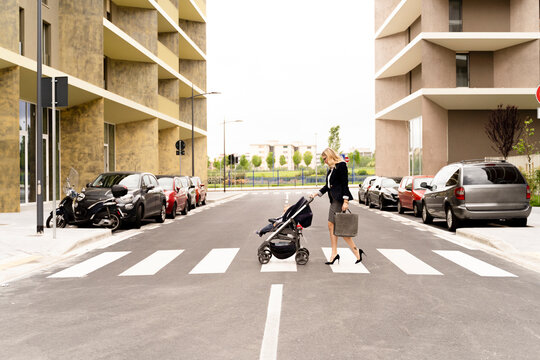 Young businesswoman with briefcase pushing stroller while crossing the street