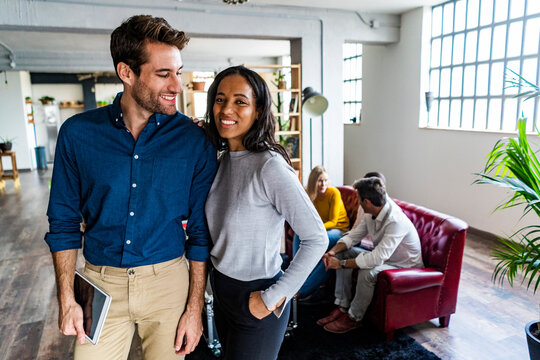 Portrait of smiling businessman and businesswoman with coworkers in background in loft office