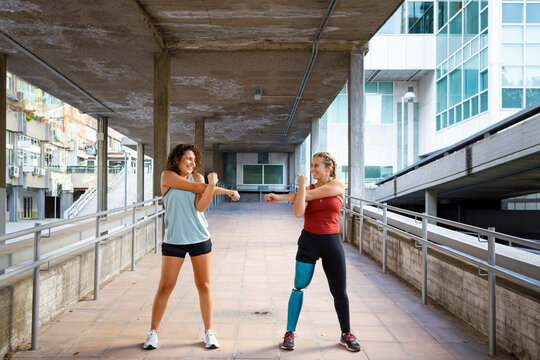 Sportswoman with prosthetic leg exercising with friend while standing on bridge