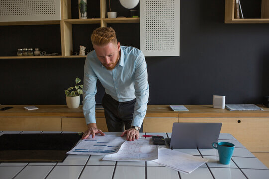 Man with laptop studying plans on table at home