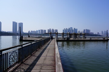 Fototapeta premium Harbor walkway with railing leading toward a city skyline over water