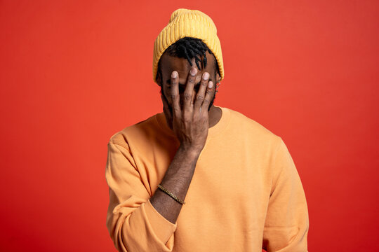 Young man covering his face in front of orange wall