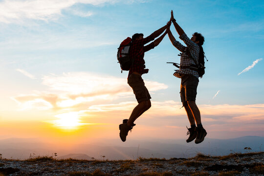 Italy, Monte Nerone, two happy and successful hikers jumping in the mountains at sunset