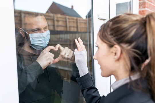 Boyfriend show heart shape gesture to girlfriend through window glass while quarantined at home
