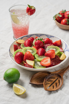 Summer brunch with fresh strawberry fruit salad and refreshing iced lemonade on table with linen tablecloth, healthy seasonal breakfast concept