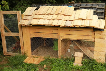 DIY wooden chicken coop with shingle roof and wire mesh enclosure in a garden setting © Delphine