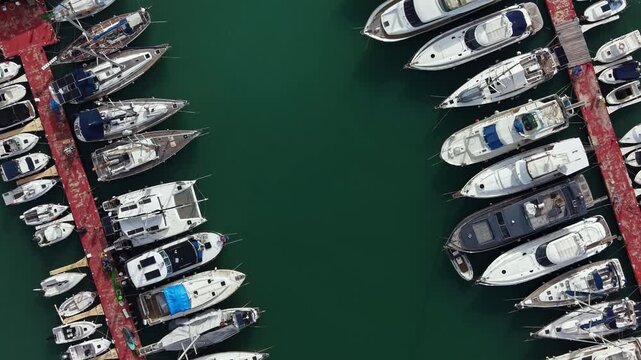 Many boats are tied at a marina. The docks are red and the water is green. This scene shows a busy area for boating. The time is during the day with good weather.