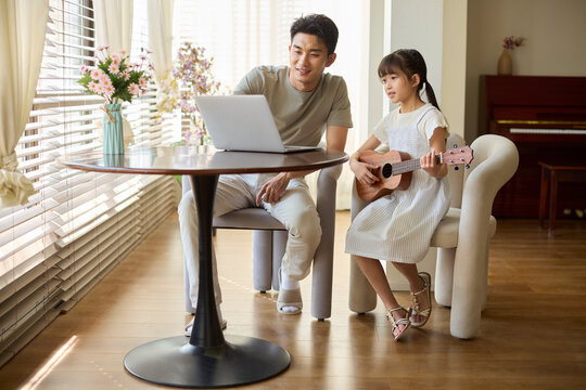 A girl following an online ukulele lesson, with her dad accompanying her
