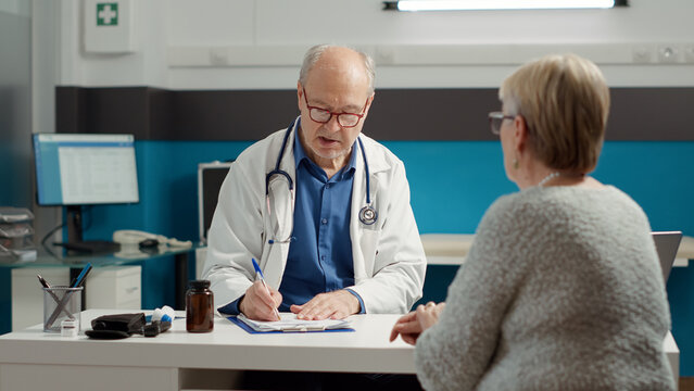 Male doctor using recovery medication to give prescription paper to retired patient in medical office. Writing information to give treatment for illness diagnosis, health care system.