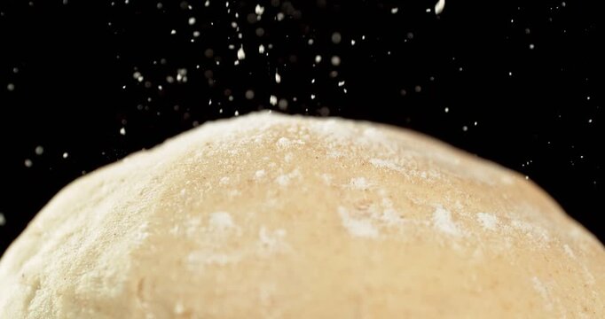 Static shot of a leavened dough loaf isolated on black background with falling flour in super slow motion, 1000 fps. Concept of baking, artisan bread making and dough preparation.