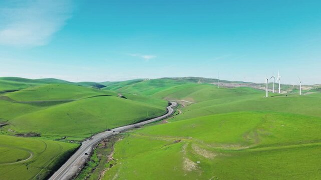Idyllic aerial perspective of the Altamont Pass wind farm, showcasing modern turbines spinning over lush green rolling hills and a winding road on a bright, clear day in northern California