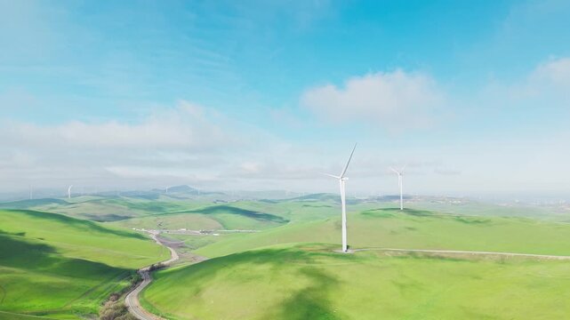 Aerial view of the Altamont Pass Wind Farm in California. Showcasing numerous wind turbines spinning across vibrant green rolling hills under a partly cloudy blue sky. A symbol of sustainable energy