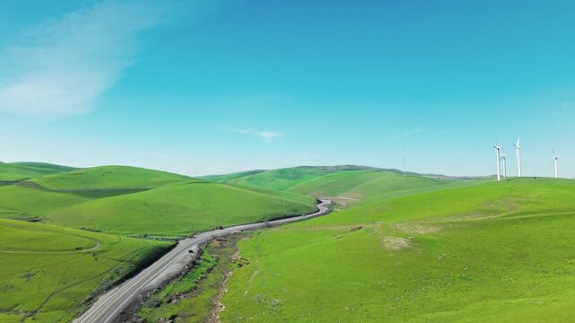 Stunning aerial footage showcasing the scenic Altamont Pass Wind Farm, with its rolling green hills, a winding road, and modern wind turbines generating clean, renewable energy