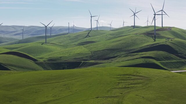 Wind turbines turning and generating clean, renewable energy over the lush green rolling hills of Altamont Pass Wind Farm in northern California, a sustainable solution to climate change
