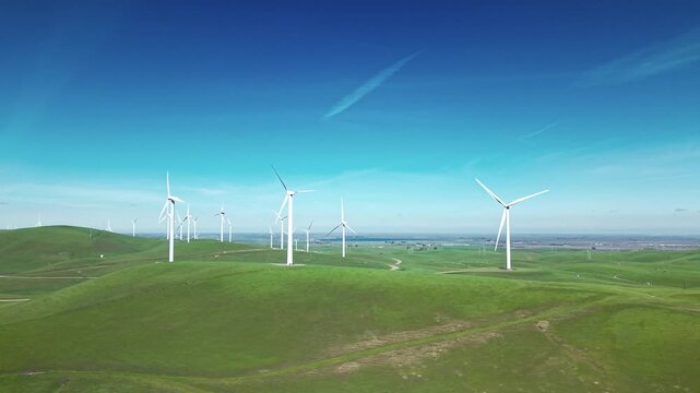 Aerial view of a wind farm on the rolling green hills of Altamont Pass, California, with turbines spinning to produce clean, sustainable energy under a clear blue sky