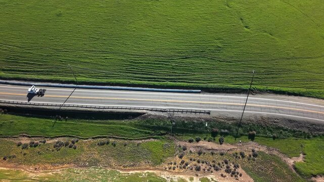 Aerial top-down view of a solitary truck driving on a rural road through verdant green fields and rolling hills on a sunny day in the California countryside near Altamont Pass