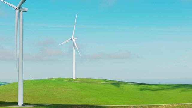 Aerial view of wind turbines spinning on vibrant green hills at the Altamont Pass Wind Farm in California, generating clean, sustainable, and renewable energy against a clear blue sky