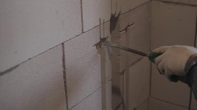 Mason Chiseling Precise Notch In Block Wall, Detailed Closeup Of Gloved Hand Guiding Chisel And Drill To Form Horizontal Channel For Conduit, Interior Renovation Scene, Careful Measured