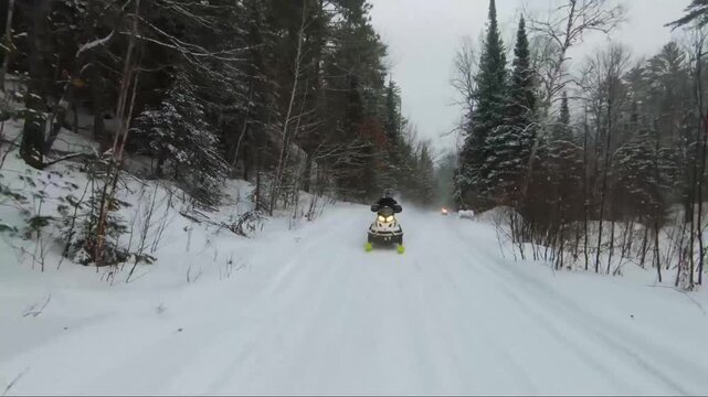 A snowmobile following through the snow covered forest roads in Quebec.