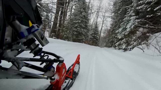 Looking down on the ski of a snowmobile in the deep snow while riding through the forest.