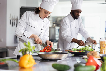 Woman chef in uniform slicing a bell pepper in professional kitchen, using fresh produce and...